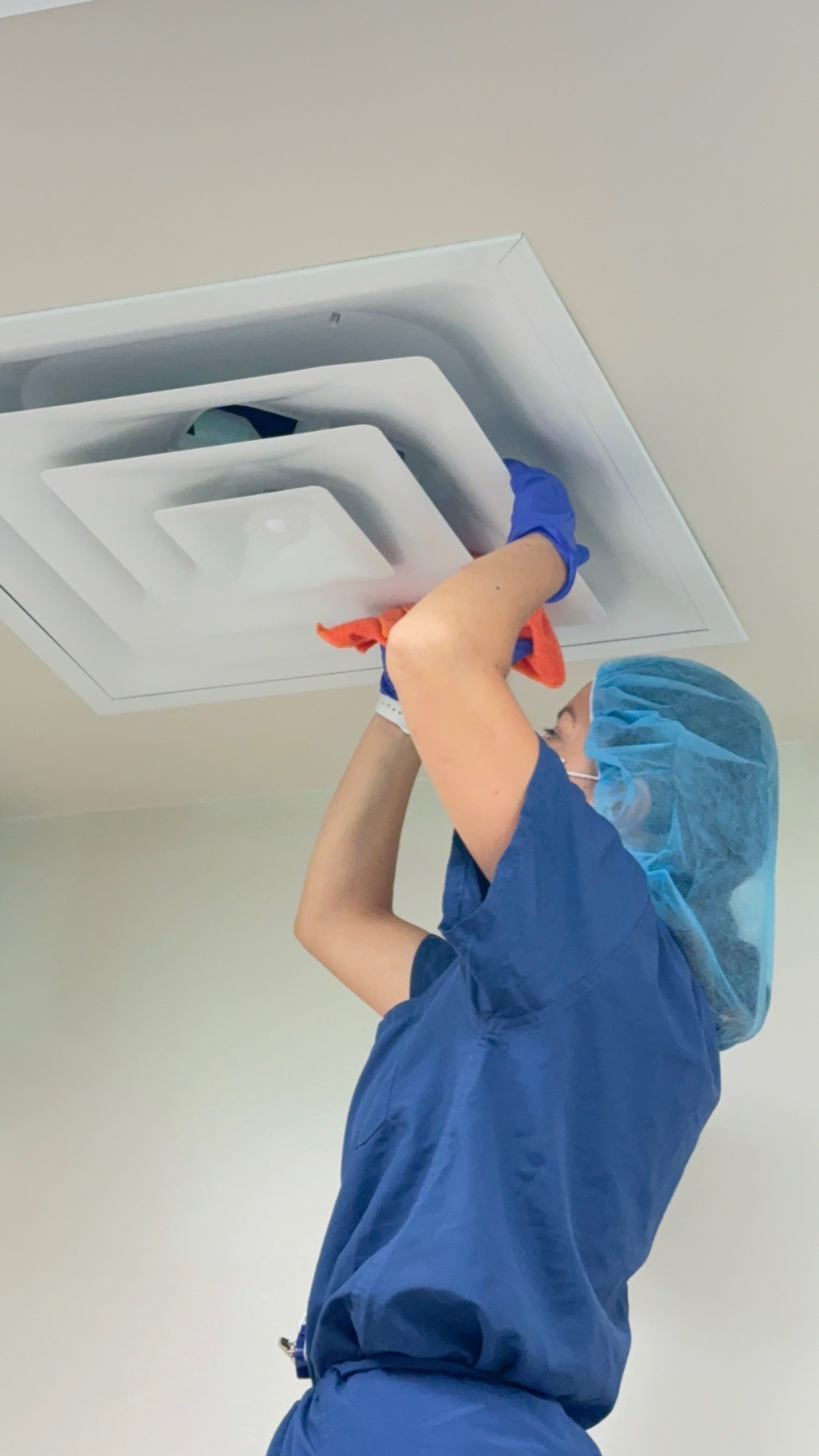 Technician wiping a ceiling air diffuser during a terminal clean